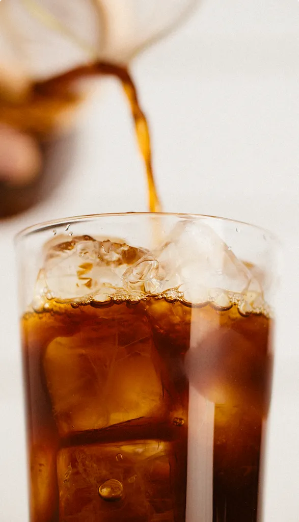 Iced coffee being poured into a glass filled with ice.