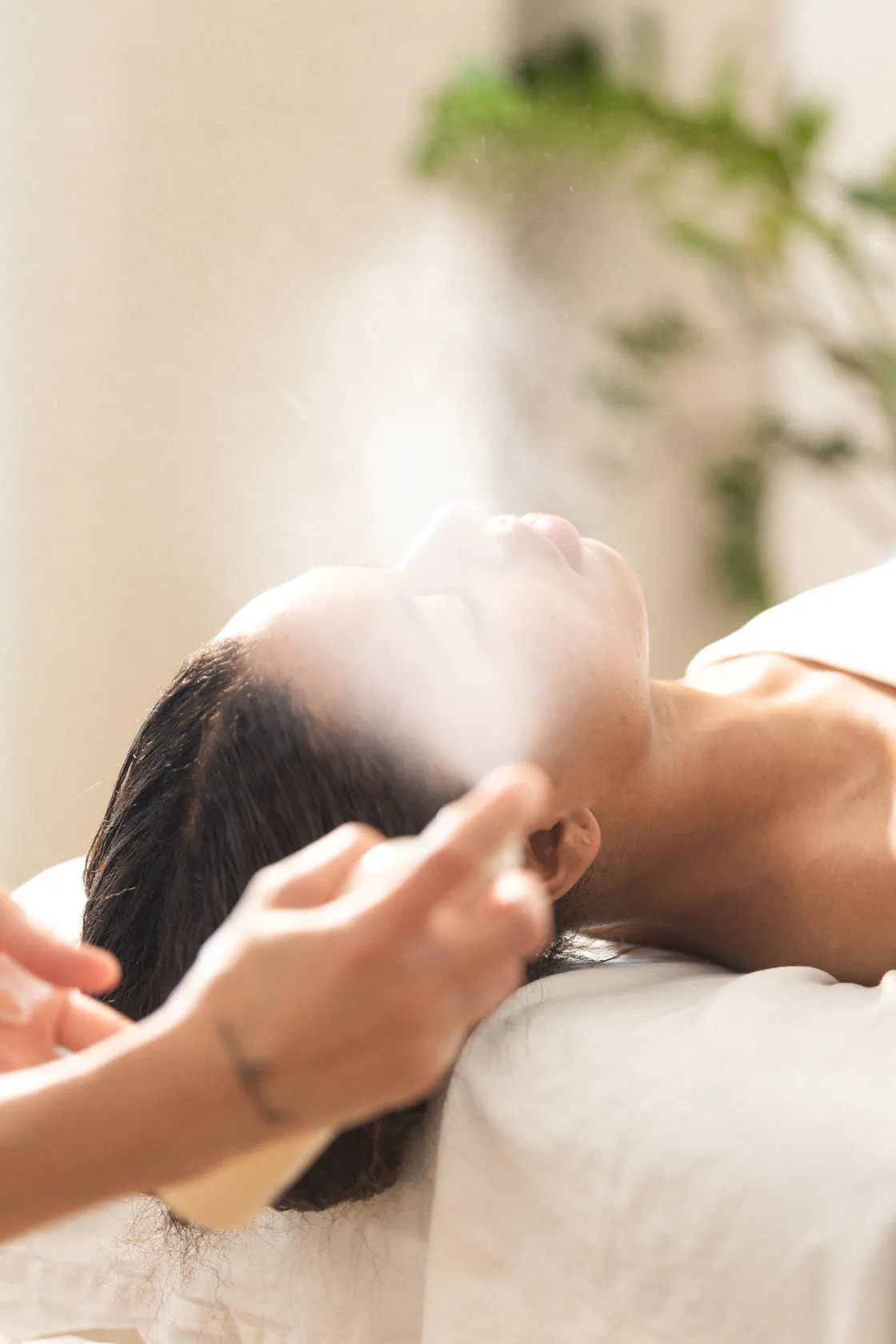 A person lying on a treatment table receives a facial mist.