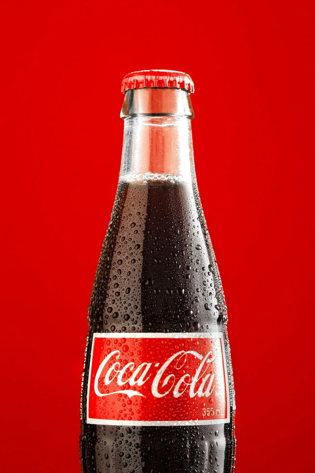 A chilled glass Coca-Cola bottle with condensation against a solid red background.