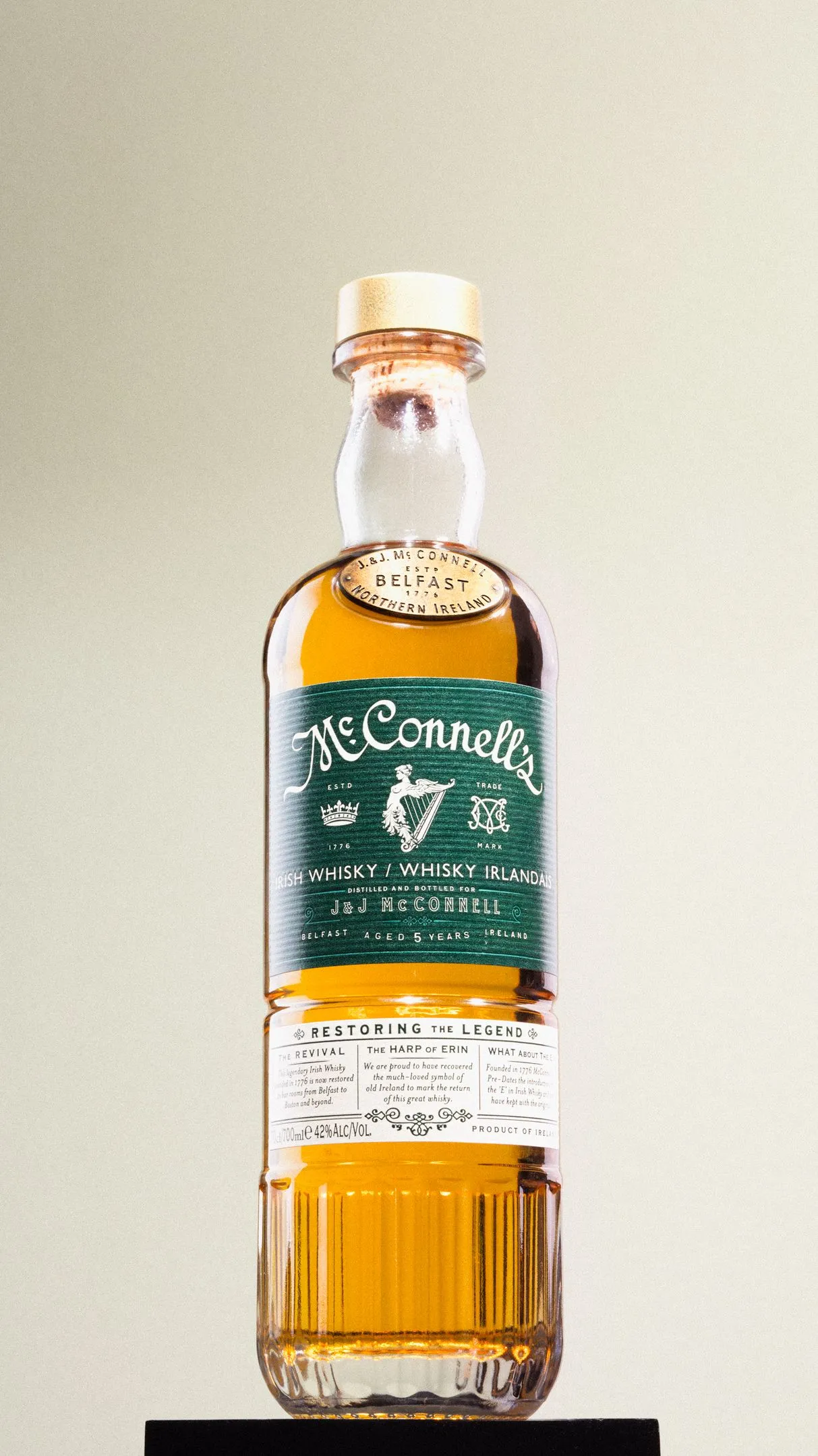 A bottle of McConnell's Irish Whiskey with a green label, filled with amber-colored liquid and sealed with a gold-colored cap.