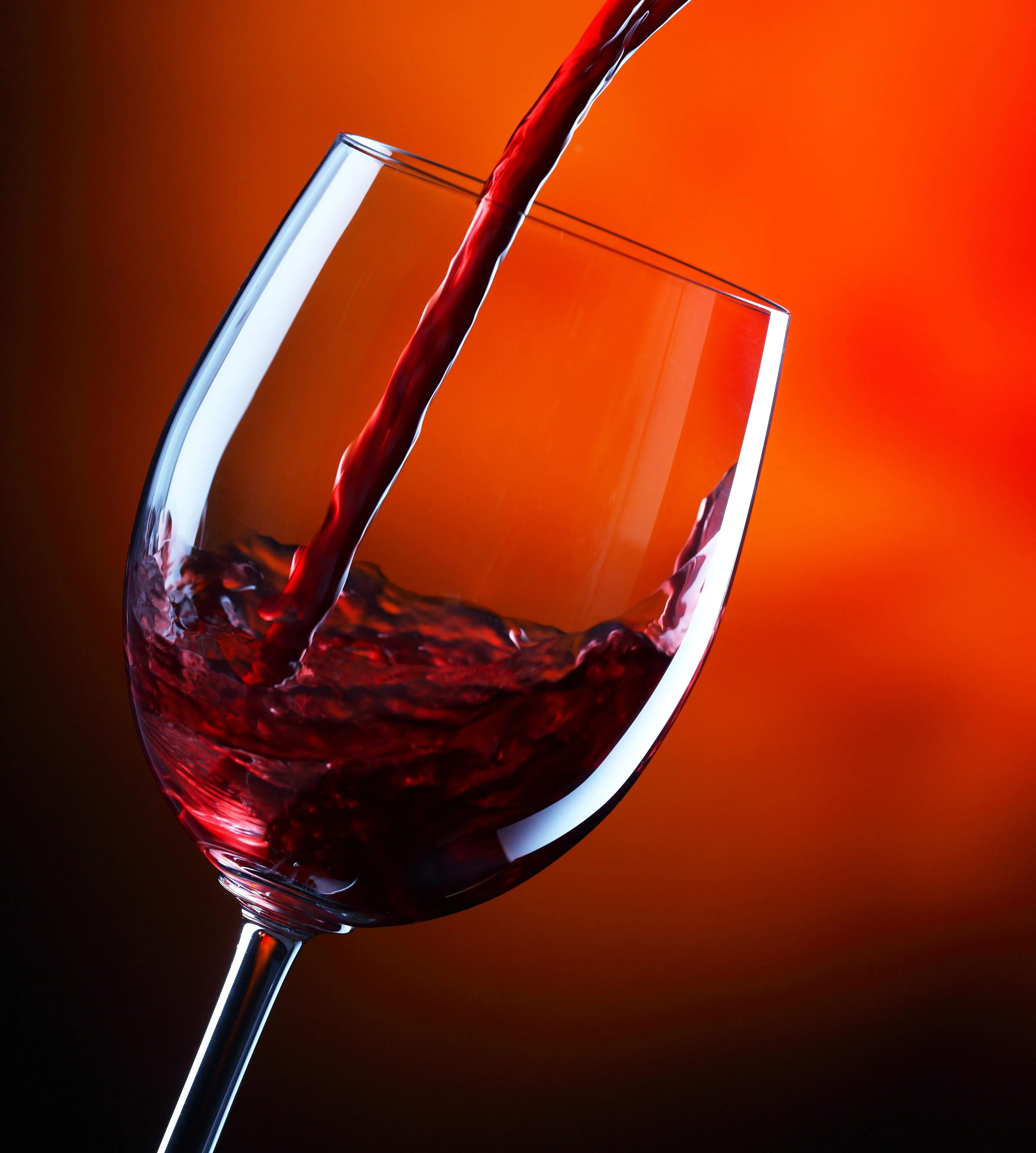 Red wine being poured into a tilted wine glass against an orange background.